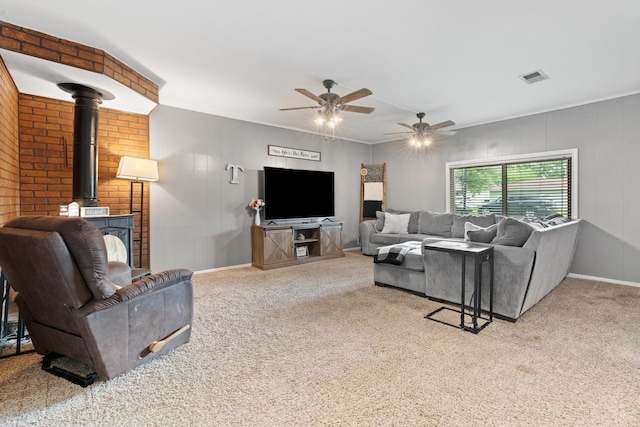 carpeted living area with ceiling fan, visible vents, baseboards, ornamental molding, and a wood stove