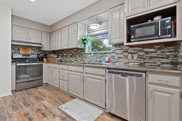 kitchen featuring sink, tasteful backsplash, stone countertops, appliances with stainless steel finishes, and light wood-type flooring