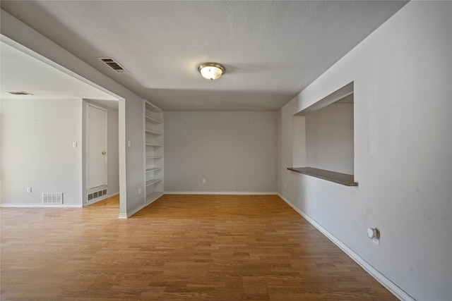 empty room with hardwood / wood-style floors, a textured ceiling, and built in shelves