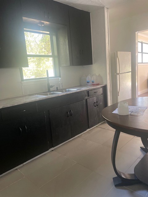 kitchen featuring light tile patterned floors, white refrigerator, a healthy amount of sunlight, and sink