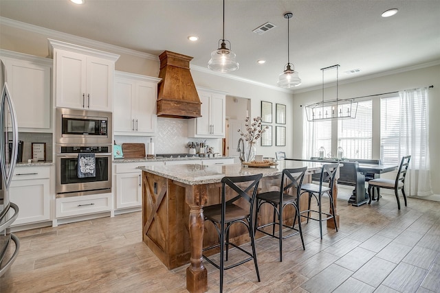 kitchen featuring an island with sink, white cabinets, appliances with stainless steel finishes, and custom range hood