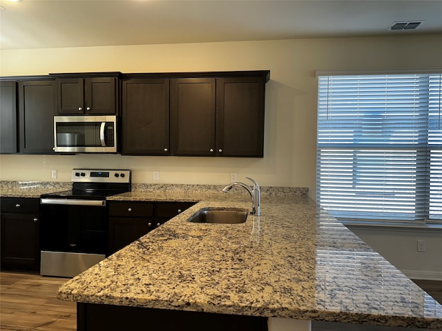 kitchen with dark brown cabinets, light wood-type flooring, light stone counters, sink, and appliances with stainless steel finishes