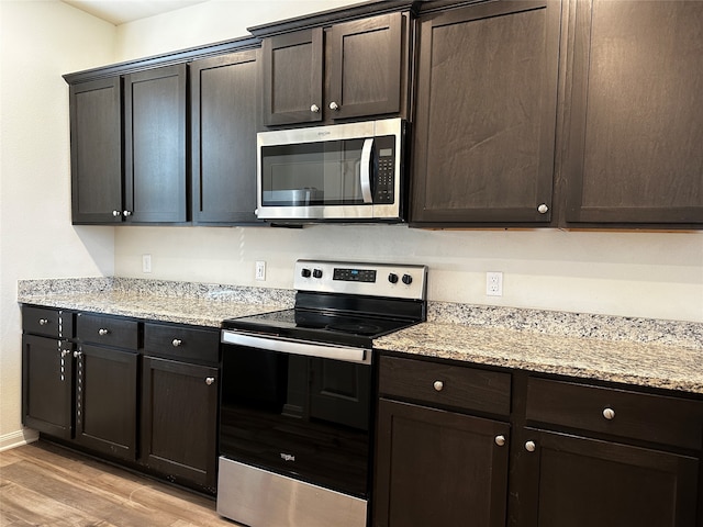 kitchen with appliances with stainless steel finishes, dark brown cabinetry, light hardwood / wood-style floors, and light stone countertops