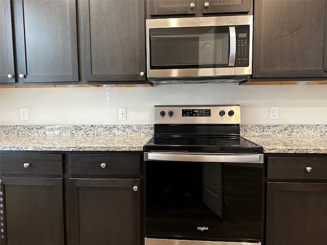 kitchen with stainless steel appliances, light stone counters, and dark brown cabinetry