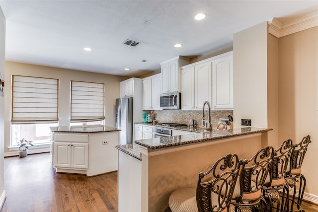 kitchen with light wood-type flooring, white cabinetry, kitchen peninsula, stainless steel appliances, and dark stone countertops