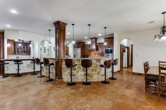 kitchen featuring hanging light fixtures, premium range hood, built in appliances, and light stone countertops