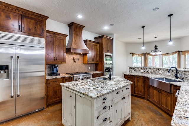 kitchen featuring custom range hood, white cabinetry, built in appliances, a center island with sink, and sink