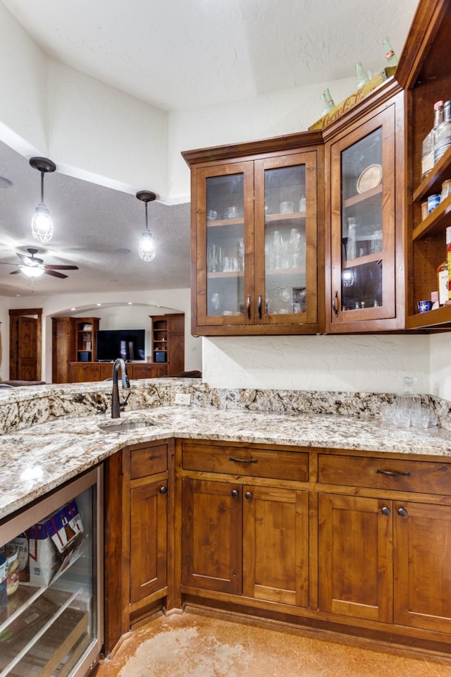 bar featuring ceiling fan, wine cooler, light stone countertops, and sink