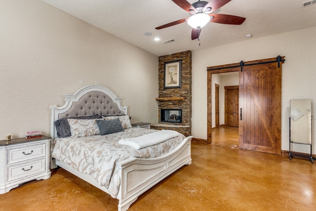 bedroom featuring ceiling fan, a stone fireplace, a textured ceiling, and a barn door