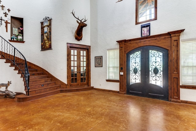 entryway with french doors, a towering ceiling, and concrete flooring