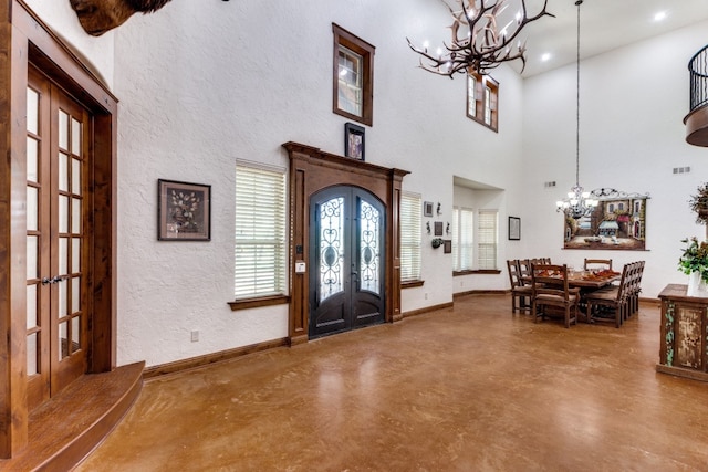 entrance foyer with an inviting chandelier, a wealth of natural light, concrete floors, and french doors