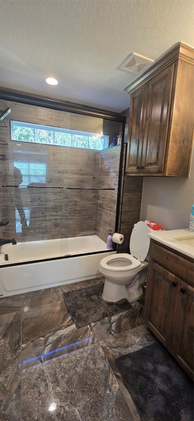 full bathroom featuring vanity, a textured ceiling, enclosed tub / shower combo, and toilet