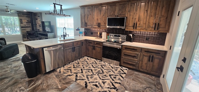 kitchen with appliances with stainless steel finishes, hanging light fixtures, kitchen peninsula, ceiling fan, and sink