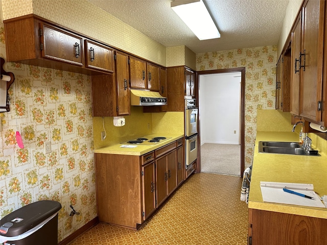 kitchen with white stovetop, a textured ceiling, double oven, sink, and light colored carpet