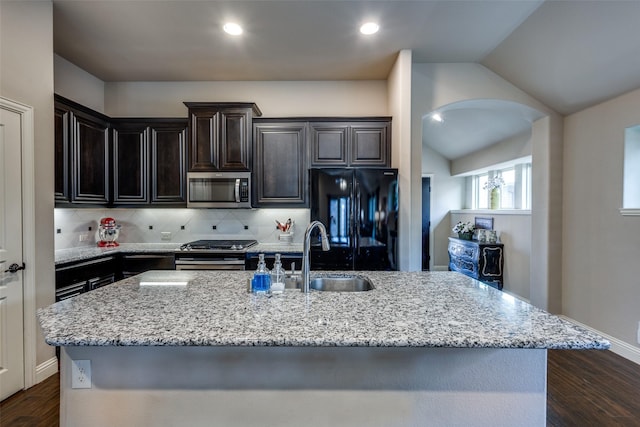 kitchen featuring dark wood finished floors, lofted ceiling, light stone counters, stainless steel appliances, and a sink