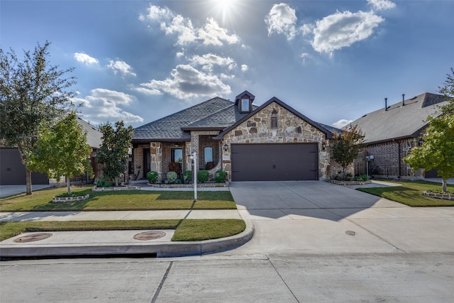 french provincial home with a garage, brick siding, driveway, stone siding, and a front yard