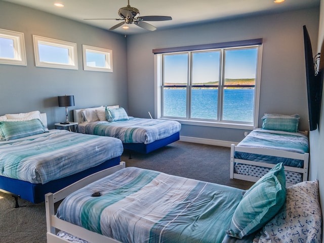 bedroom with multiple windows, a water view, dark colored carpet, and ceiling fan