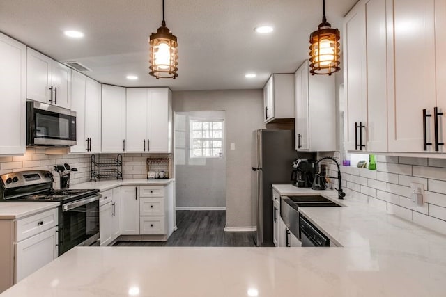 kitchen with appliances with stainless steel finishes, hanging light fixtures, light stone countertops, and white cabinets