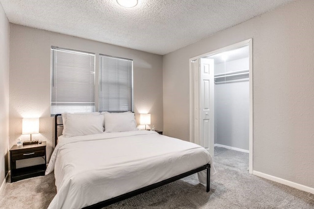 bedroom with a closet, a textured ceiling, a walk in closet, and carpet flooring