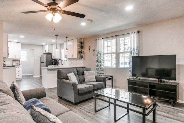 living room with light wood-type flooring, a textured ceiling, sink, and ceiling fan