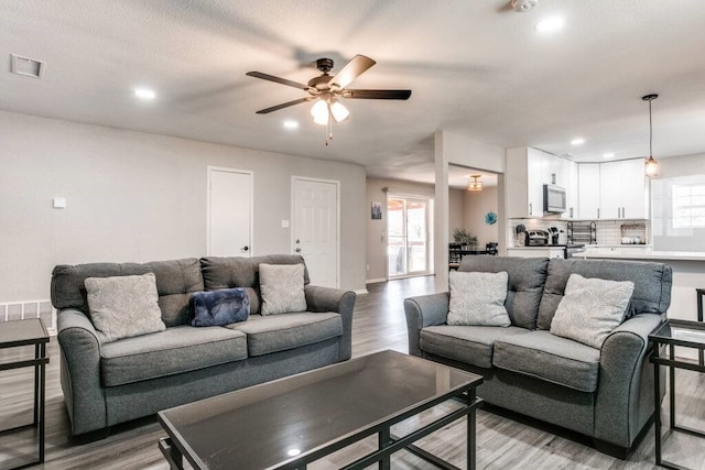 living room with light hardwood / wood-style floors, ceiling fan, and a textured ceiling