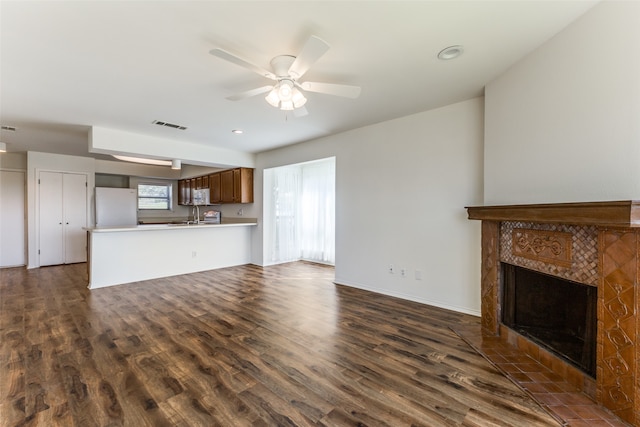 unfurnished living room with a tiled fireplace, ceiling fan, dark hardwood / wood-style floors, and sink