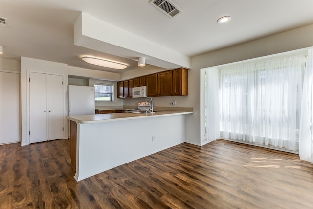 kitchen featuring white appliances, kitchen peninsula, dark hardwood / wood-style floors, and sink