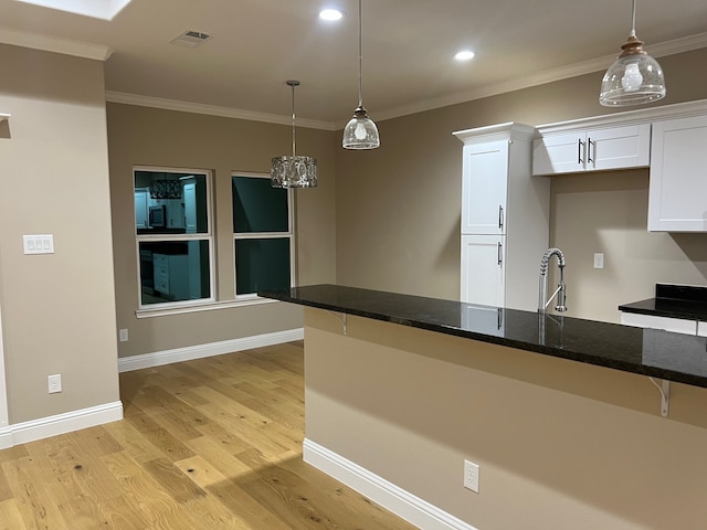 kitchen with dark stone counters, light hardwood / wood-style floors, white cabinetry, hanging light fixtures, and ornamental molding