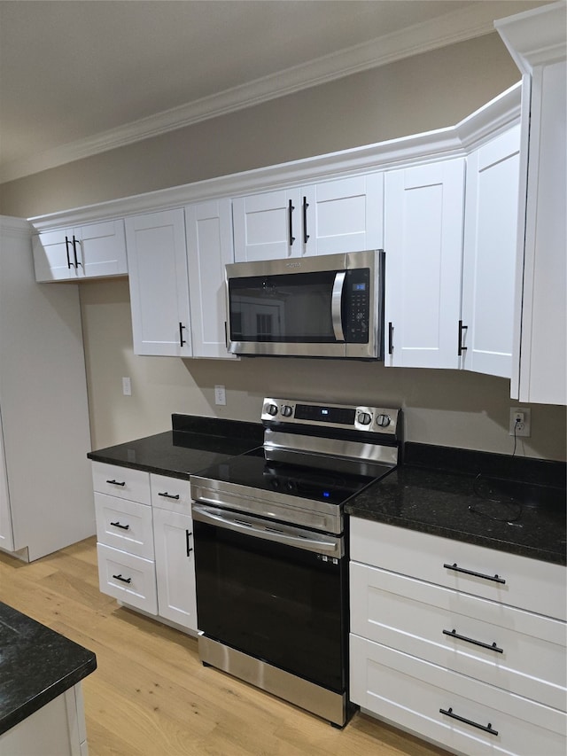 kitchen with light hardwood / wood-style flooring, white cabinetry, appliances with stainless steel finishes, dark stone countertops, and crown molding