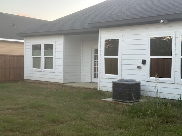 back house at dusk featuring a yard and central AC