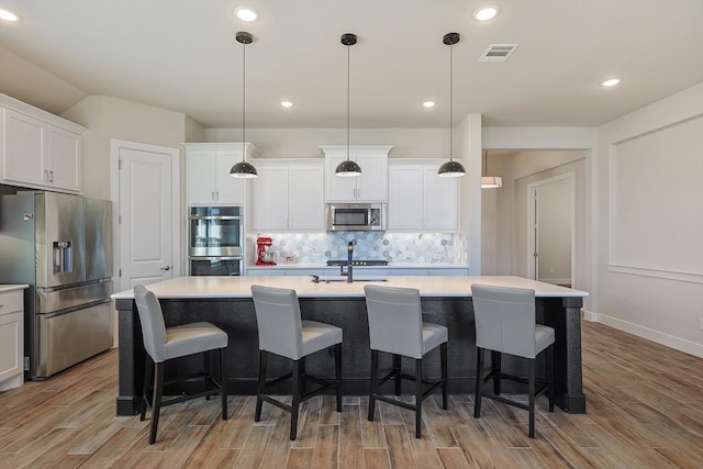 kitchen with white cabinetry, stainless steel appliances, light hardwood / wood-style floors, decorative light fixtures, and a kitchen island with sink