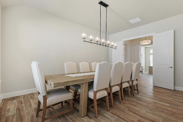 dining room featuring hardwood / wood-style floors, an inviting chandelier, and vaulted ceiling