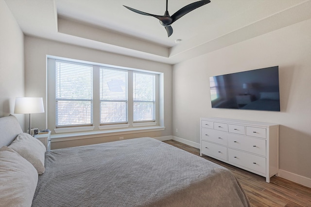 bedroom featuring hardwood / wood-style floors, a tray ceiling, multiple windows, and ceiling fan