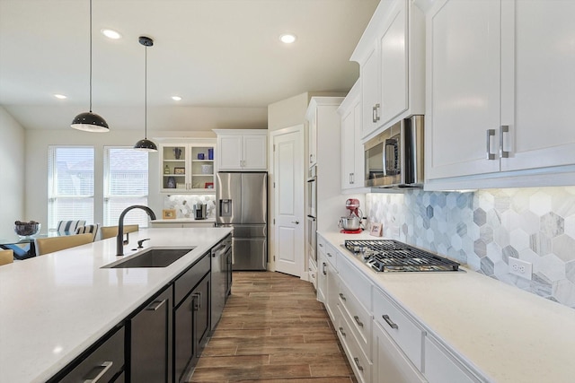 kitchen with stainless steel appliances, sink, wood-type flooring, decorative light fixtures, and white cabinetry