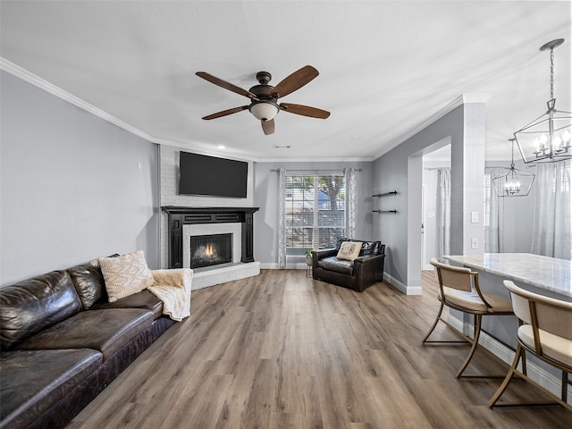 living room featuring wood-type flooring, ceiling fan with notable chandelier, a fireplace, and ornamental molding