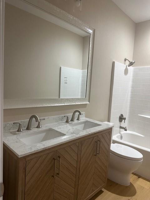 1008 S Preston St, Ennis, TX 75119 - full bath featuring double vanity, toilet, wood finished floors, and bathing tub / shower combination