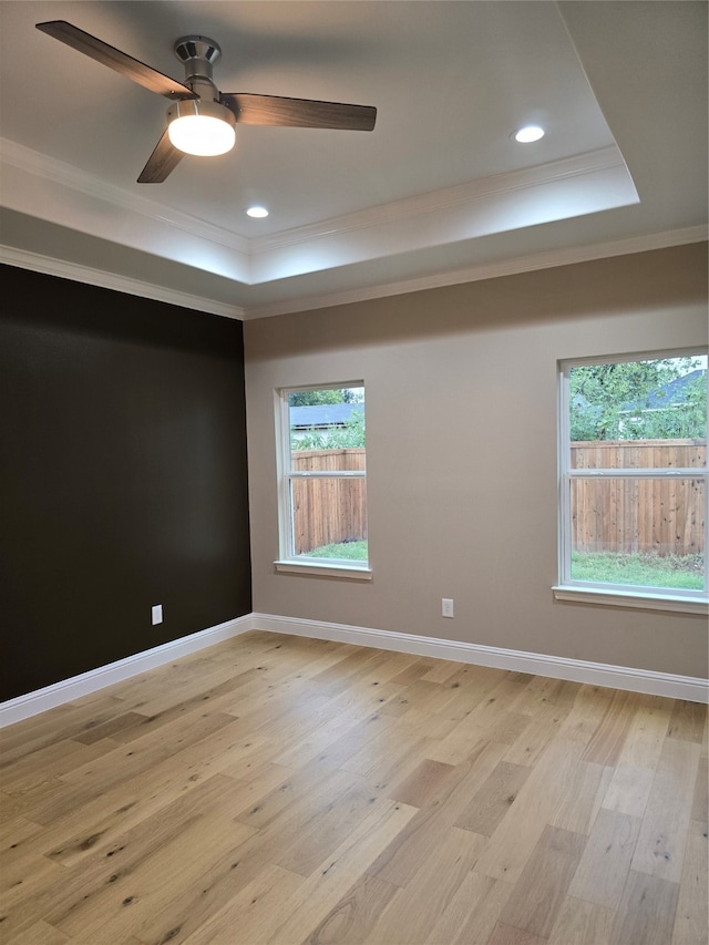 empty room with a raised ceiling, light hardwood / wood-style floors, ornamental molding, and ceiling fan