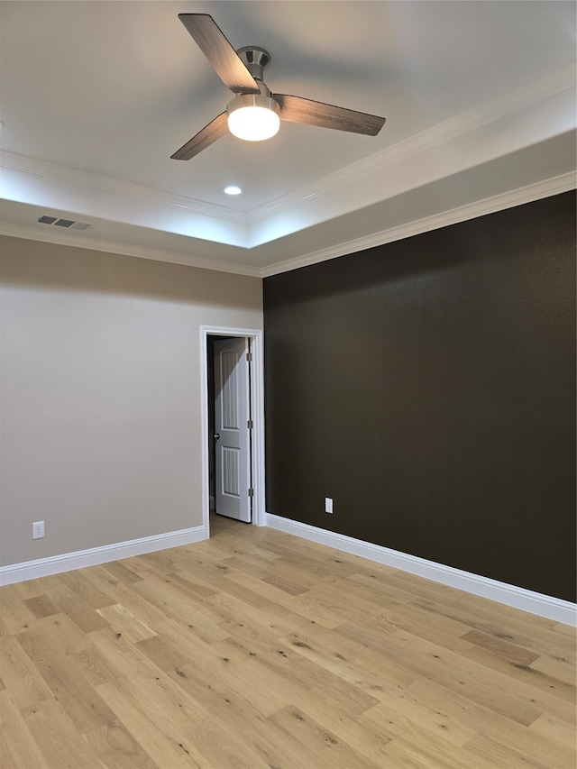 unfurnished room featuring a raised ceiling, ornamental molding, ceiling fan, and light hardwood / wood-style flooring