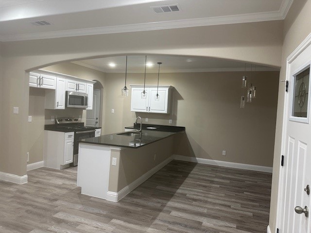 kitchen with appliances with stainless steel finishes, white cabinets, kitchen peninsula, decorative light fixtures, and hardwood / wood-style floors