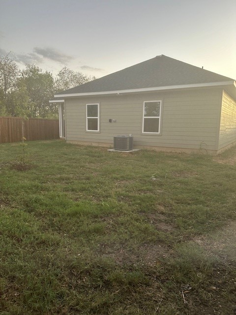 back house at dusk with a yard and central air condition unit