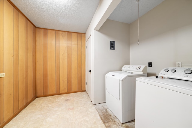 clothes washing area with a textured ceiling, wooden walls, and washer and dryer