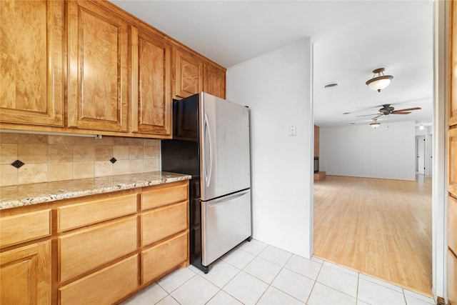 kitchen featuring ceiling fan, stainless steel fridge, tasteful backsplash, light hardwood / wood-style flooring, and light stone countertops