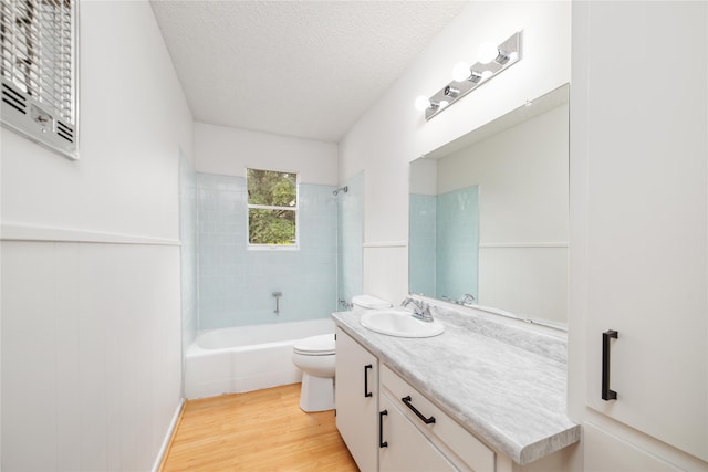 full bathroom with tiled shower / bath, vanity, a textured ceiling, hardwood / wood-style flooring, and toilet