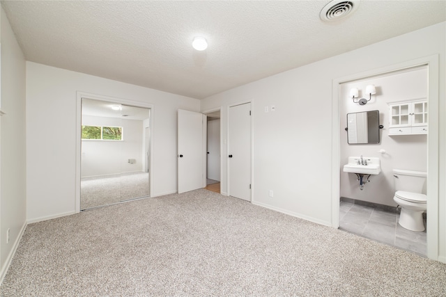 unfurnished bedroom with a textured ceiling, ensuite bath, sink, and light colored carpet