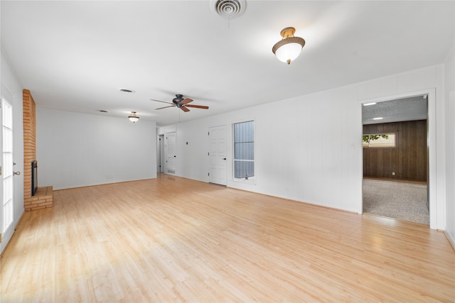 empty room with wood walls, light hardwood / wood-style floors, a fireplace, and ceiling fan