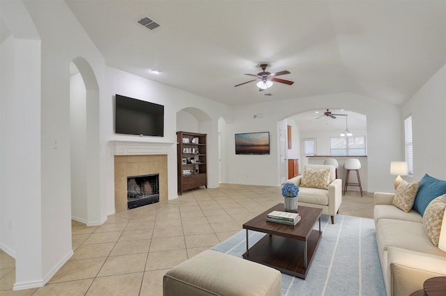 living room featuring a fireplace, light tile patterned flooring, vaulted ceiling, and ceiling fan