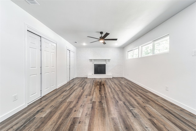 unfurnished living room with ceiling fan, brick wall, dark hardwood / wood-style floors, and a fireplace