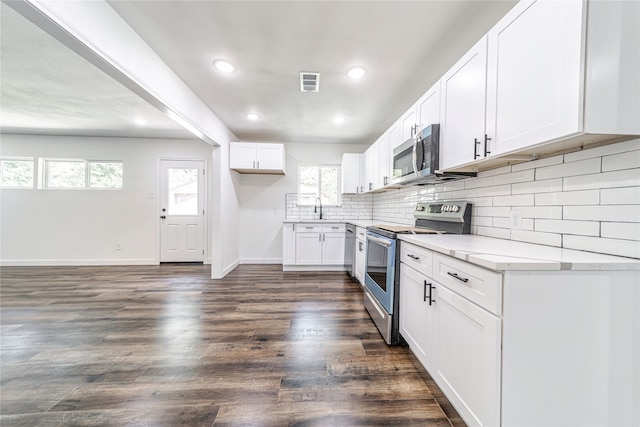 kitchen featuring sink, backsplash, white cabinetry, appliances with stainless steel finishes, and dark hardwood / wood-style floors