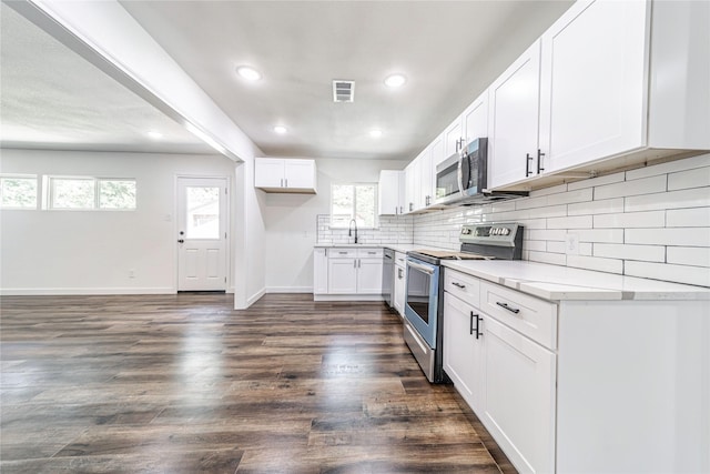 1504 Nichols St, Ennis, TX 75119 - kitchen with appliances with stainless steel finishes, decorative backsplash, light countertops, dark wood-style flooring, and white cabinetry