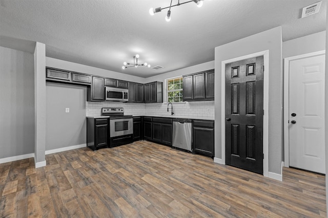 kitchen with tasteful backsplash, stainless steel appliances, a textured ceiling, an inviting chandelier, and dark hardwood / wood-style floors